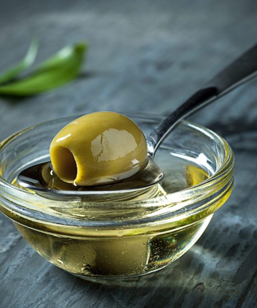 Olive oil and olive branch on the gray wooden table as background